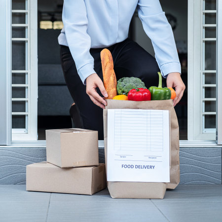 Asian man customer in quarantine time order food delivery online and courier place grocery bag of food, fruit, vegetable and parcel on front of the door without contact to reduce   infectionの写真素材