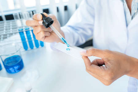 Close up of scientist woman holding dropper to dropping solution sample on the glass plate for...