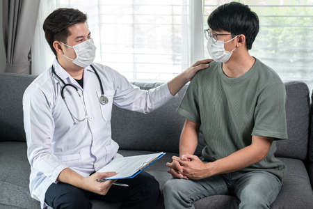 Man doctor in medical face mask holding document clipboard to discussion about result heath examination and encourage to patient  during medical help at homeの写真素材