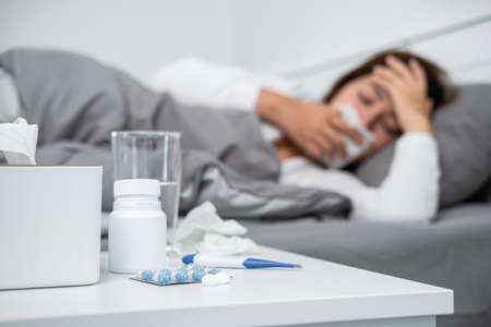 Asian woman using tissue to cough, sneezing and touching forehead while feeling sick and lying in...