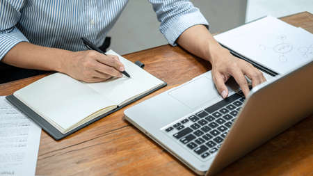 Business woman reading business report to checking financial data on laptop and writing information...