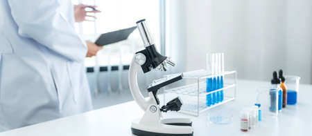 Scientist woman standing to reading result coronavirus vaccine on report after using microscope and...