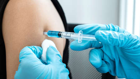 Doctor in medical glove holding syringe and using cotton before injection coronavirus vaccine in shoulder of patient to protection from covid-19 pandemic during doctor made an appointment at hospitalの写真素材