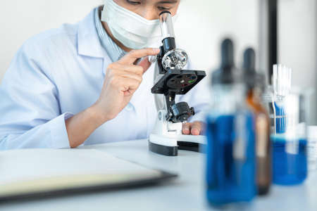 Scientist woman using microscope to analyzing and development coronavirus vaccine while working with...