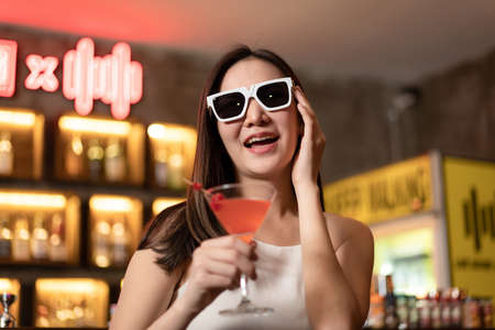 Beautiful woman is wearing sunglasses and drinking cocktail during having enjoy to relaxing while...