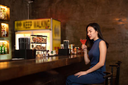 Beautiful woman is drinking cocktail and having enjoy to relaxing while sitting alone to listening music on counter bar in restaurant or hotel barの写真素材