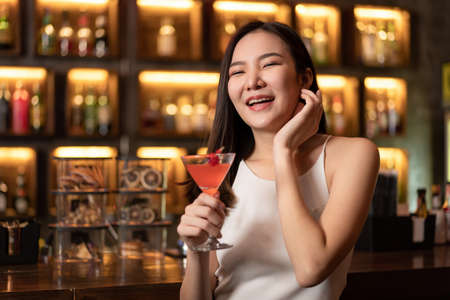 Beautiful woman is drinking orange cocktail and having enjoy to relaxing while smiling and sitting alone to listening music on counter bar in restaurant or hotel barの写真素材