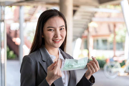Asian businesswoman in suit, preparing to wearing protective face mask to protection from during outbreak virus when working at outside officeの写真素材