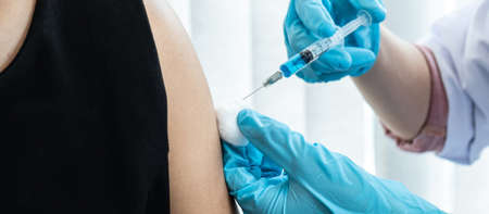 Doctor in medical glove holding syringe to injection virus vaccine in the shoulder of patient to...