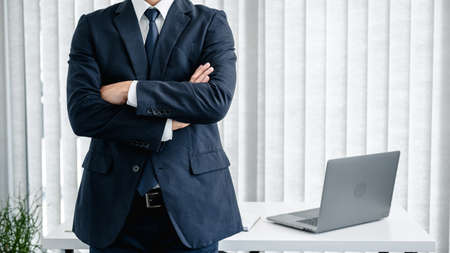 Cropped image of businessman in suit standing with arms crossed and feeling confidence in work about new business project while looking at the camera in the room at officeの写真素材
