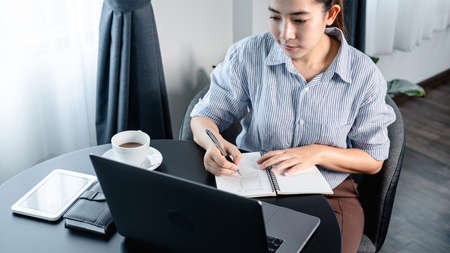Businesswoman looking on laptop screen to reading financial report and writing information on...
