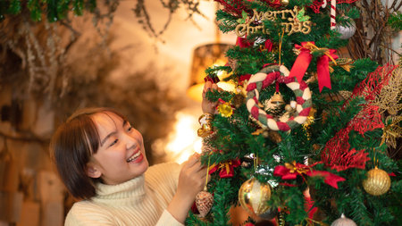 Happy beautiful woman in sweater holding santa boots and decoration to decorate on christmas tree for celebration christmas or new year in living room at homeの写真素材