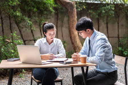 Young business woman and businessman talking and looking financial report on document to discussion about marketing plan while sitting at outdoor officeの写真素材