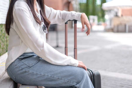 Woman traveller sitting holding dragging black suitcase luggage while walking to passenger boarding in airport, Travel concept.の写真素材