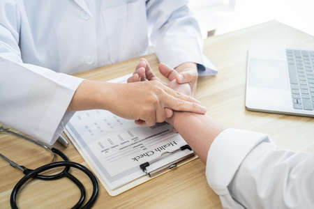 Doctor in white coat taking and checking the patient's wrist pulse during the examination diagnosis...