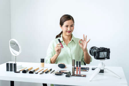 Female beauty blogger is showing lipstick to reviewing product and showing use to makeup cosmetics while recording videos for streaming on her blogの写真素材