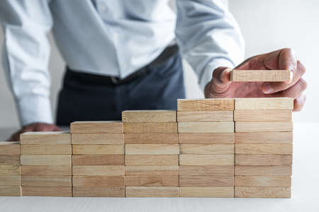 Risk To Make Business Growth Concept With Wooden Blocks, hand of businessman has piling up and...