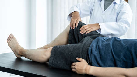 Female physiotherapist doing healing treatment and rehabilitation injured knee of patient by...