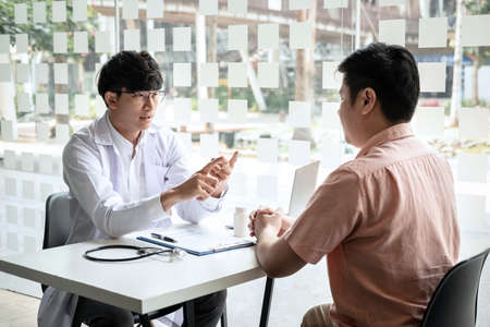 Male doctor discussing with the patient explaining symptoms of the disease after diagnosis checking while recommending treatment methods in clinic.の写真素材