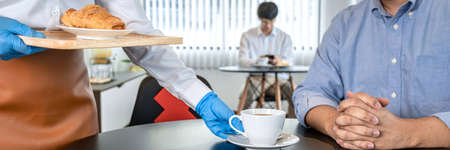 Close up of asian woman waitress serving coffee and bread to client while wearing face mask and face...