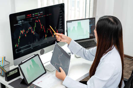 Businesswoman investor working with computer, tablet and analyzing graph stock market trading...