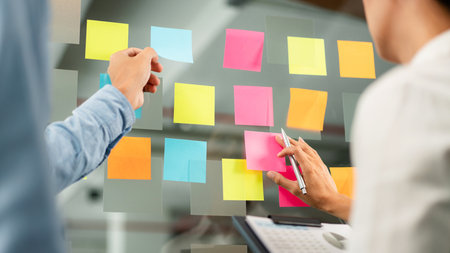Two business executive team holding and taking notes keyword on board wall to brainstorm about a new...