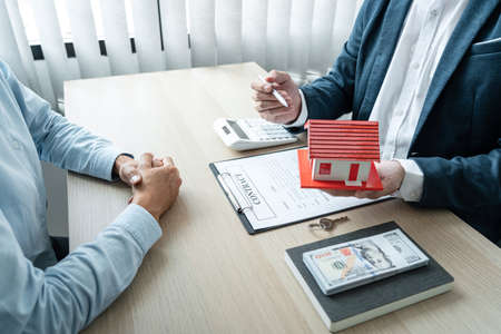 Real estate broker agent consulting the customer to a decision making sign insurance form contract, home model mortgage loan offer for and house insurance.の写真素材