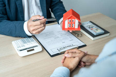 Real estate broker agent consulting the customer to a decision making sign insurance form contract, home model mortgage loan offer for and house insurance.の写真素材