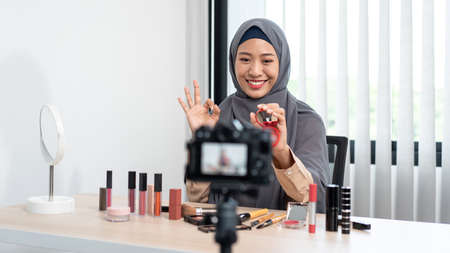 Woman muslim blogger is showing present make up tutorial beauty cosmetic review product and broadcast live streaming video to social network teaching online on the camera screen.の写真素材