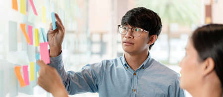 Two business executive team holding and taking notes keyword on board wall to brainstorm about a new business project for planning marketing plan together in the office.の写真素材