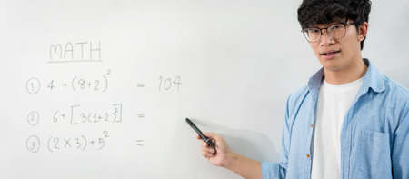 Male tutor standing in front of whiteboard and writing math equations on board to explaining new lesson while talking on e-learning class online by live streaming videoの写真素材