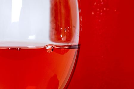 Extreme close up of rose wine in clear glass with bubble and bottle in background