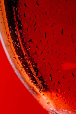 Macro close up of side of wine glass with red or rose wine and droplets of water and the bottle in the backgroundの写真素材