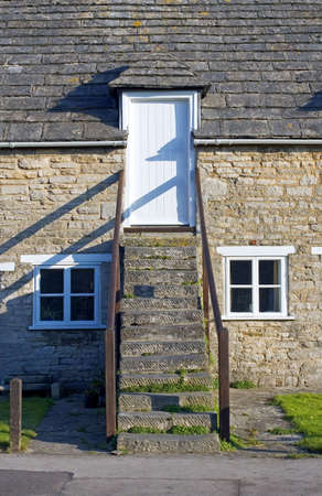 Traditional stone clad house with stone steps leading to the road on a sunny day in Corfe, Dorset,...