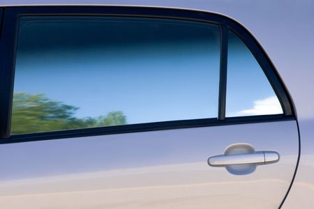 Clean lines and shades of a car door and window with reflection of trees, sunny blue sky and cloudsの写真素材