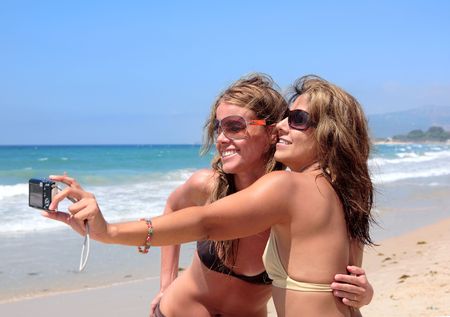 Two young women taking photos of each other on a sunny beach