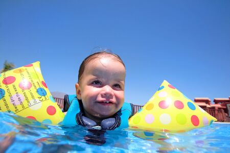  girl floating on top of swimming pool in flotation jacket and arm bands