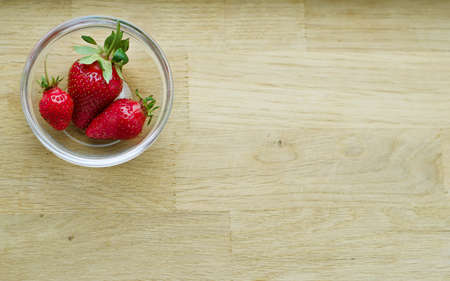 An overhead shot of strawberries in a glass bowl on a wooden background.の写真素材