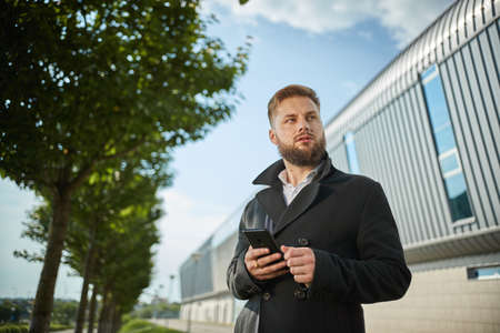 Portrait of seductive young man holding black jacket collar while standing, posing with both hands, stylish male pulling his jacket collar, outside, arrangingの写真素材