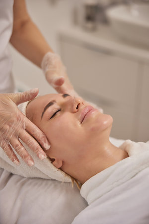 cosmetology clinic, Female cosmetologist, contouring massage. Female cosmetologist meticulously offers face massage to client inside beauty establishment.の写真素材