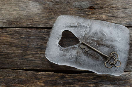 Old key in a block of ice with a heart on the old boardsの写真素材