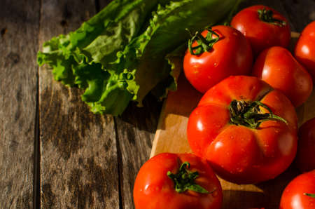 Ripe tomatoes on a cutting Board and salad leaves on old tableの写真素材