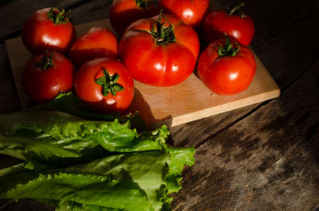Ripe tomatoes on a cutting Board and salad leaves on old tableの写真素材