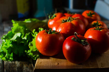 Ripe tomatoes on a cutting Board and salad leaves on old tableの写真素材