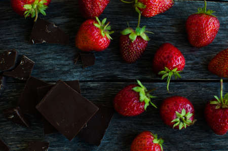 Strawberries and pieces of broken chocolate on the old wooden background