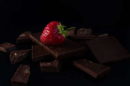 One strawberry in broken chocolate bar on a black backgroundの写真素材