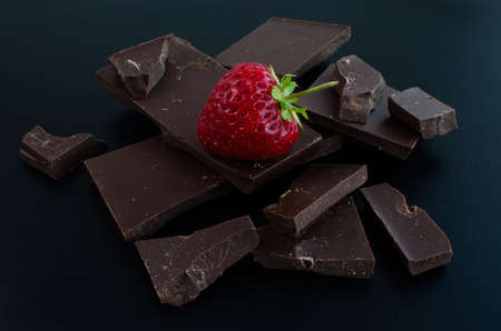One strawberry in broken chocolate bar on a black background
