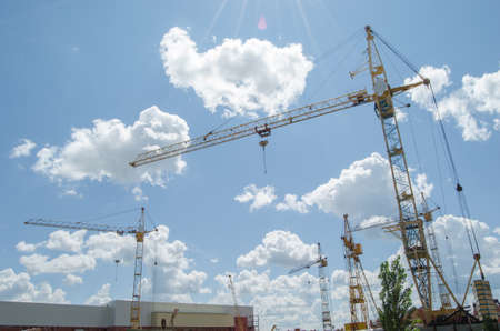 Construction cranes on background of blue cloudy sky in a construction site