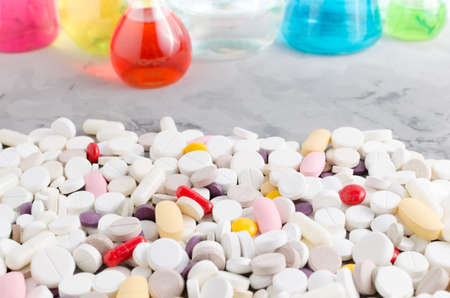 A large variety of medicinal pills on the background of vials and flasks filled with liquid