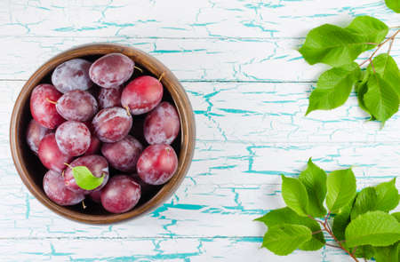 Plums in wooden bowl with green leaves on the table in the sunの写真素材